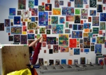 woman's outstretched arms in front of a cluster of small paintings on a white wall